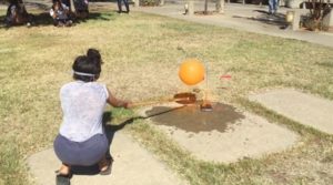 outside, a woman kneeling with a flame under a balloon