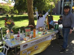 outside, a table of chemistry experiments with student presenters around the table