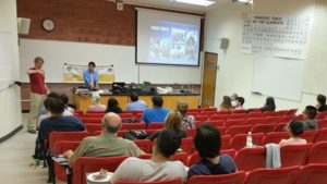 Students in a classroom with two speakers at the front of the room