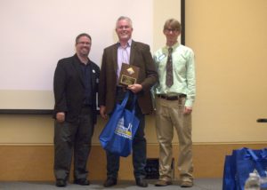 three people, center one holding award